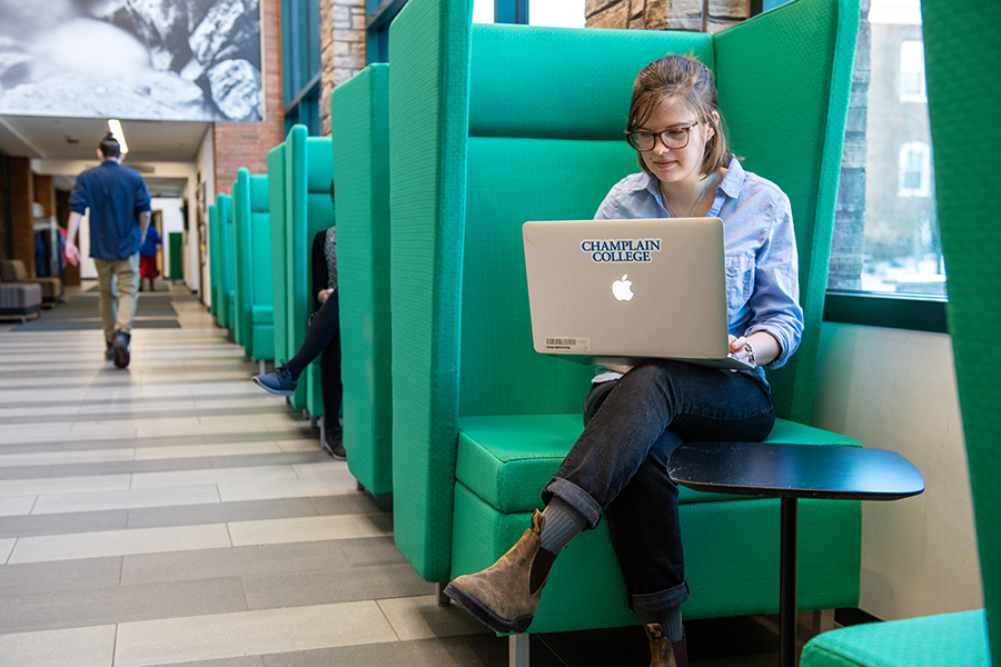 A student sits in CCM's green chairs on a laptop at Admitted Student Day.