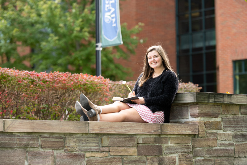 Professional Writing major Haley Seymour sits on a campus bench taking notes.