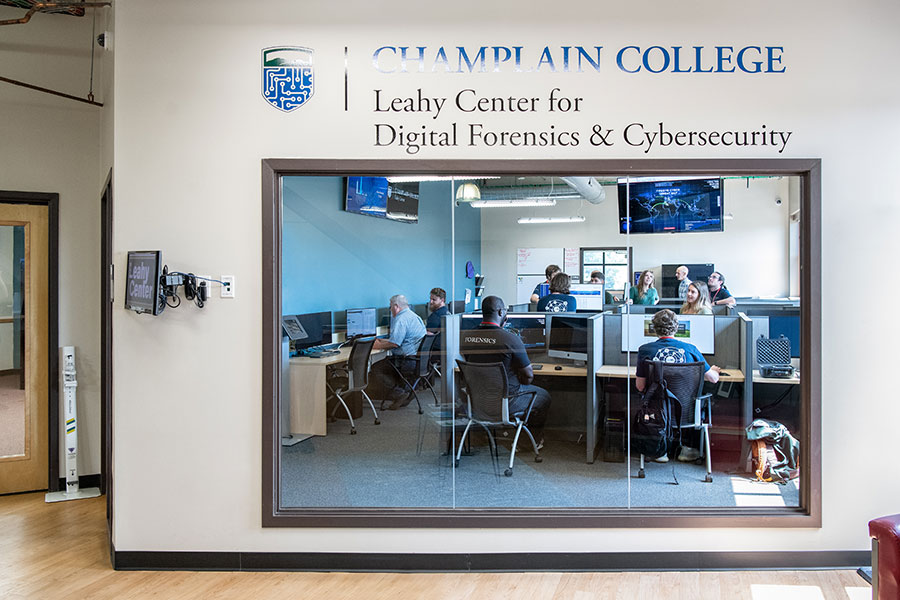 An exterior glass wall of the Leahy Center for Digital Forensics and Cybersecurity at Champlain College reveals students working diligently at computer stations. 