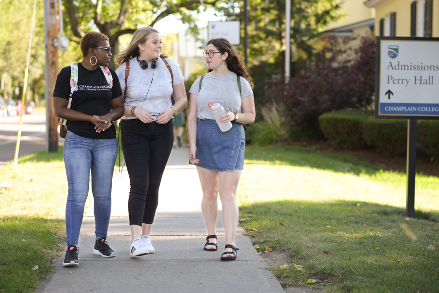 Three students walk together along a sidewalk at Champlain College.