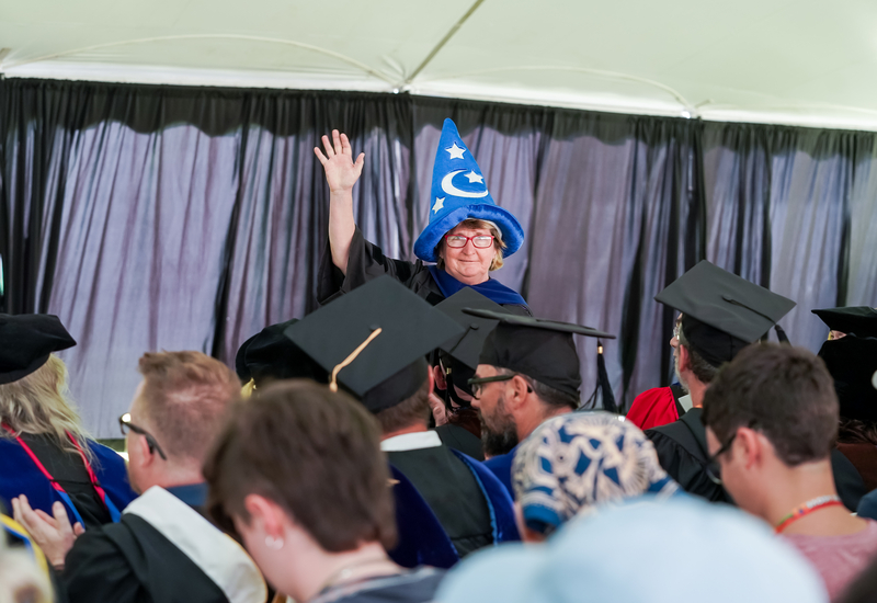 Dr. Kimberly Quinn wears a blue wizard hat and waves to a crowd of people.