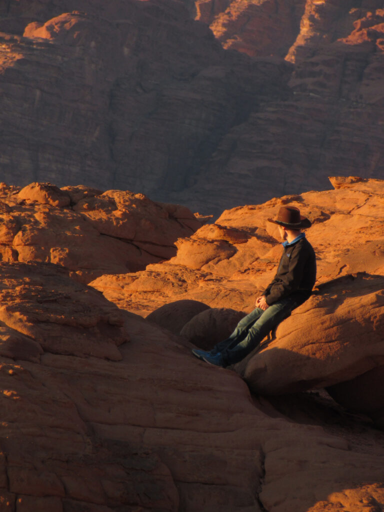 A student wearing a cowboy hat overlooks the view in Jordan, close to sunset.